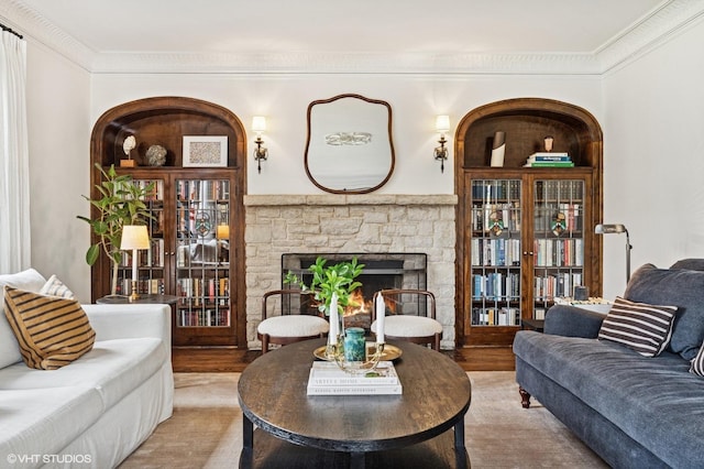 living room featuring wood finished floors, a stone fireplace, and crown molding
