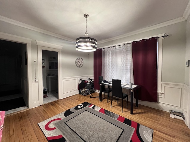 interior space featuring crown molding, a notable chandelier, wainscoting, light wood finished floors, and a decorative wall