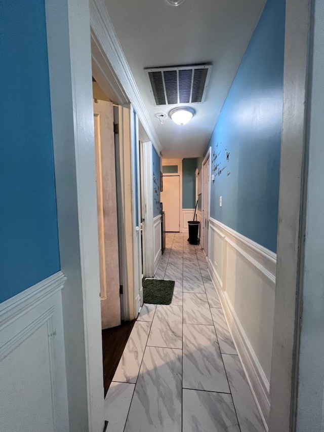 hall featuring a wainscoted wall, a decorative wall, marble finish floor, and visible vents