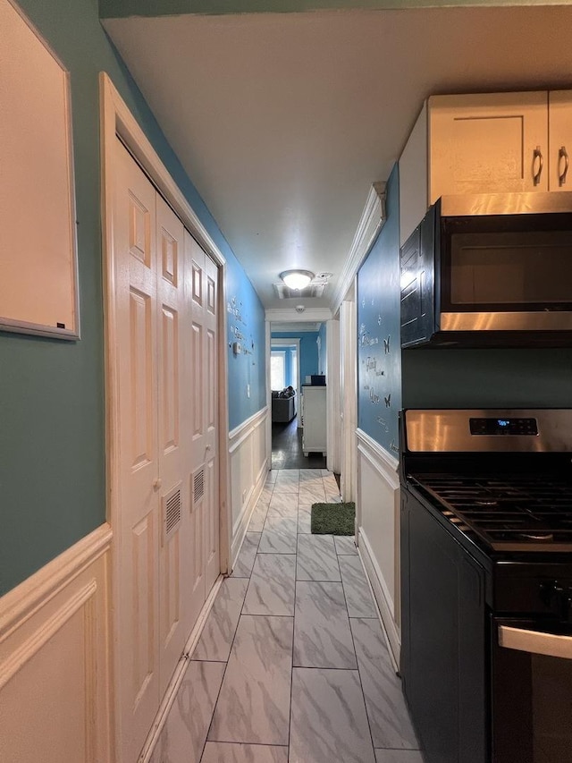 hallway with a decorative wall, visible vents, wainscoting, and marble finish floor