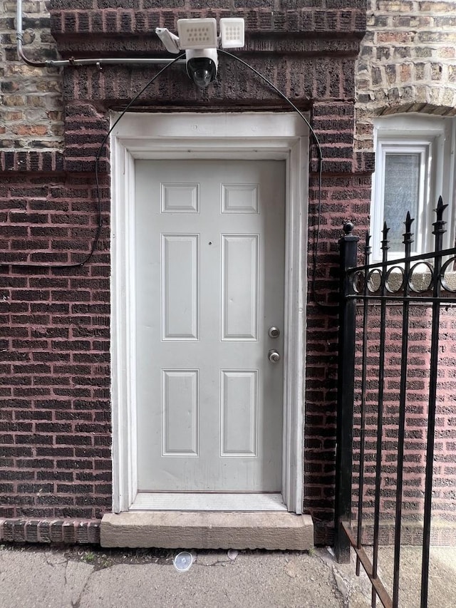 view of exterior entry with brick siding and fence
