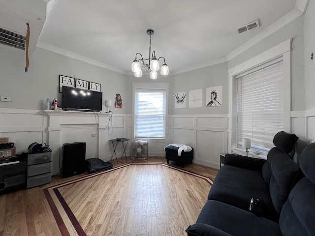 living room featuring ornamental molding, a decorative wall, wood finished floors, and visible vents