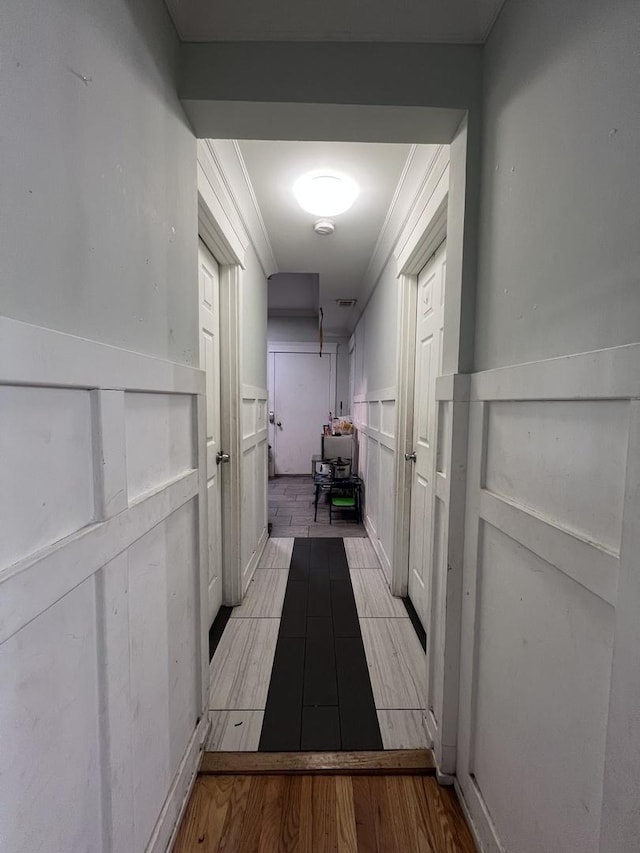 hallway with crown molding, wainscoting, a decorative wall, and visible vents