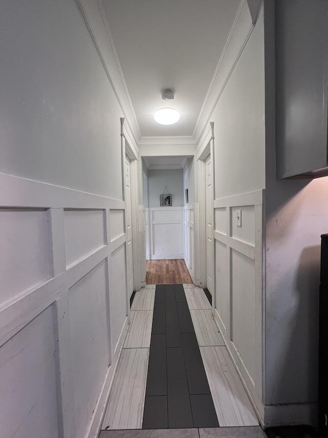 hallway featuring crown molding, light wood-type flooring, built in features, and a decorative wall