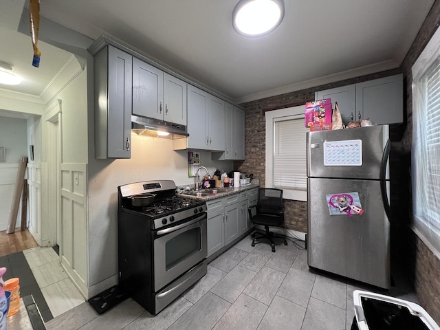 kitchen featuring crown molding, gray cabinets, under cabinet range hood, a sink, and appliances with stainless steel finishes