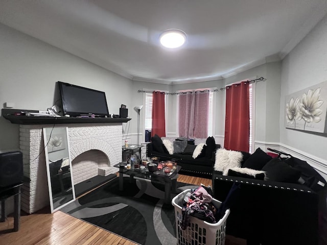 living room featuring a brick fireplace, ornamental molding, and wood finished floors