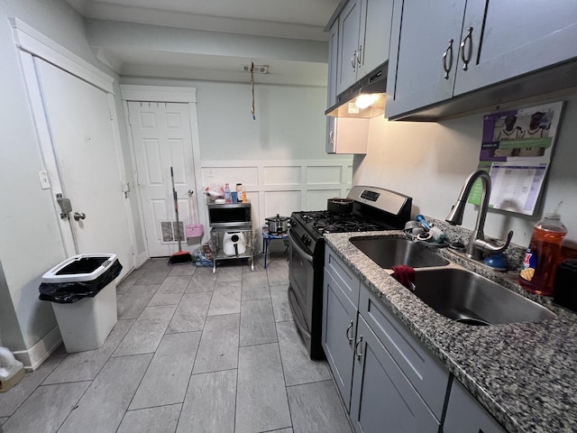 kitchen featuring under cabinet range hood, gray cabinets, a sink, and stainless steel gas stove