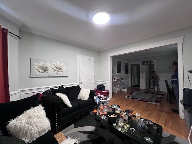 living area featuring crown molding, a decorative wall, wood finished floors, and a wainscoted wall