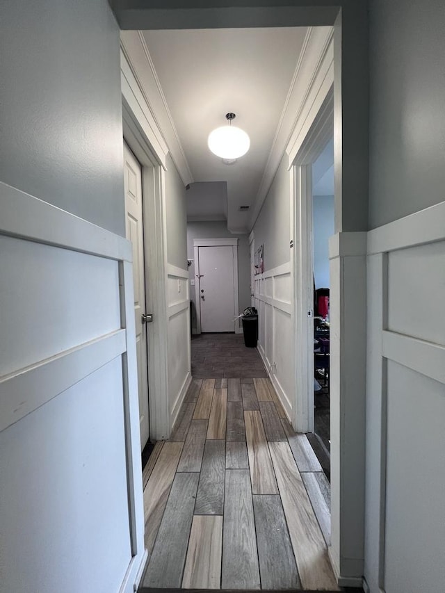 corridor featuring wainscoting, ornamental molding, wood finished floors, and a decorative wall