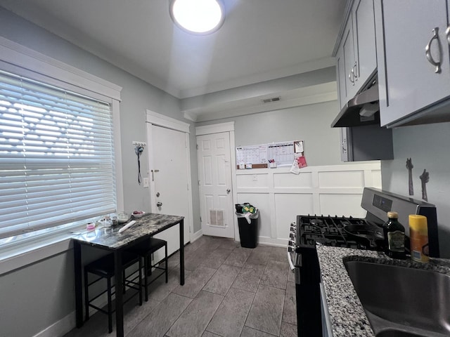kitchen with a sink, stainless steel range with gas stovetop, under cabinet range hood, and visible vents