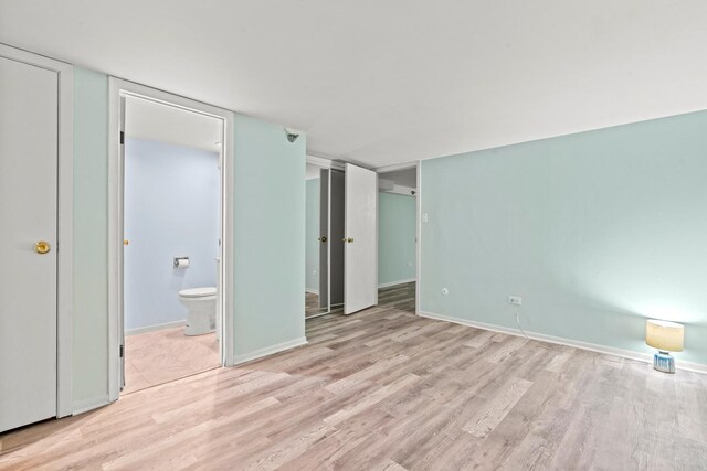 unfurnished bedroom featuring baseboards, wood finished floors, and ensuite bath