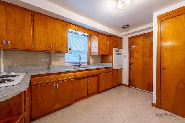 kitchen featuring white appliances, brown cabinets, a sink, and tasteful backsplash
