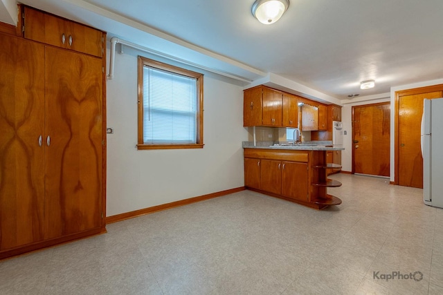 kitchen featuring brown cabinetry, light countertops, a sink, freestanding refrigerator, and a peninsula