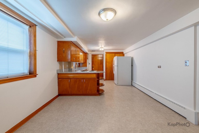 kitchen featuring brown cabinetry, freestanding refrigerator, a peninsula, baseboards, and a baseboard heating unit