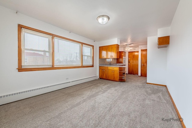 kitchen with brown cabinetry, light countertops, baseboards, a baseboard radiator, and light carpet