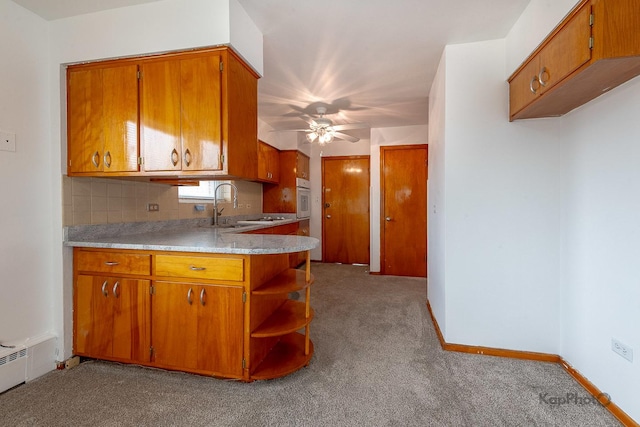 kitchen with light countertops, a ceiling fan, brown cabinetry, and carpet
