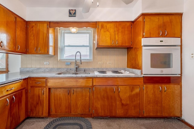kitchen with white appliances, backsplash, brown cabinets, and a sink