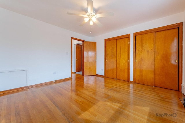 unfurnished bedroom featuring two closets, baseboards, ceiling fan, and light wood-type flooring