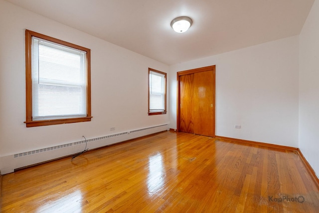 empty room with baseboards, light wood finished floors, and baseboard heating
