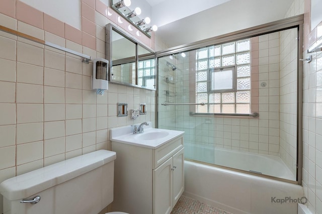 bathroom with shower / bath combination with glass door, vanity, toilet, tile patterned floors, and tile walls