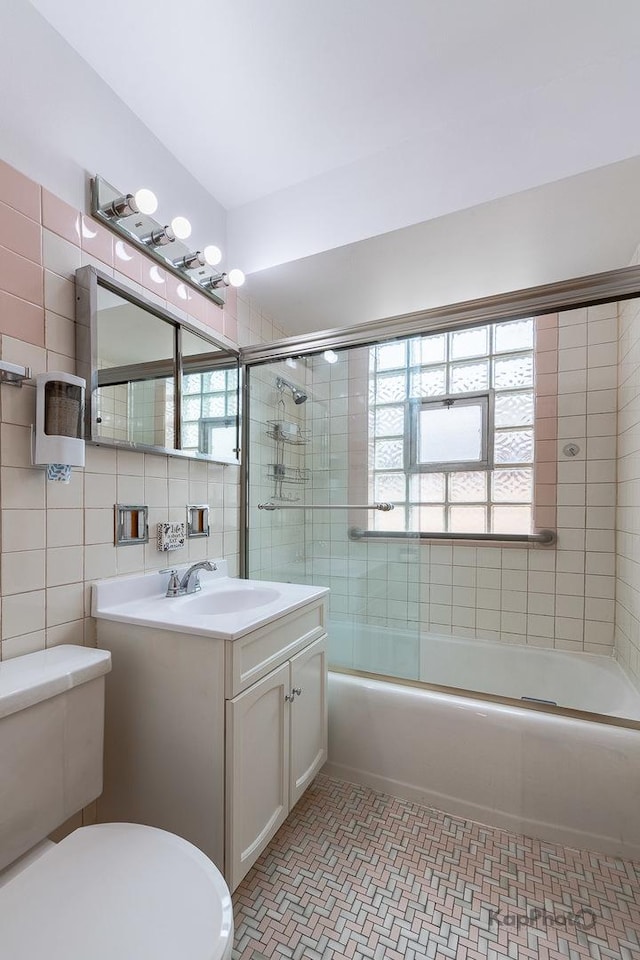 full bath featuring vanity, combined bath / shower with glass door, toilet, and a wealth of natural light
