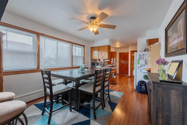 dining space featuring ceiling fan, baseboard heating, and light wood finished floors