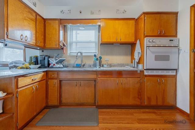 kitchen featuring light wood-style floors, a sink, backsplash, and white oven