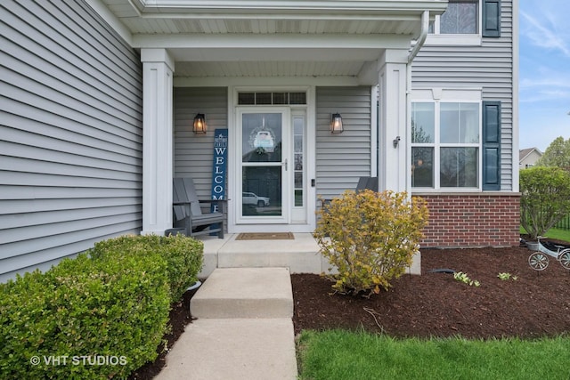 view of exterior entry with a porch and brick siding