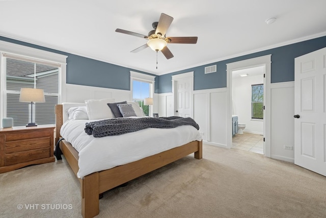 bedroom featuring visible vents, wainscoting, light carpet, and a decorative wall