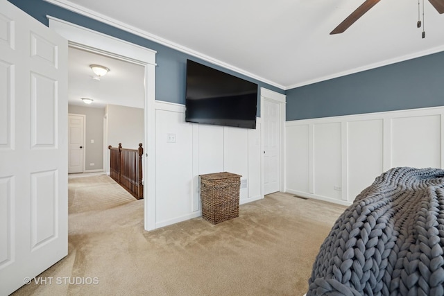 bedroom featuring crown molding, light colored carpet, a wainscoted wall, and a decorative wall