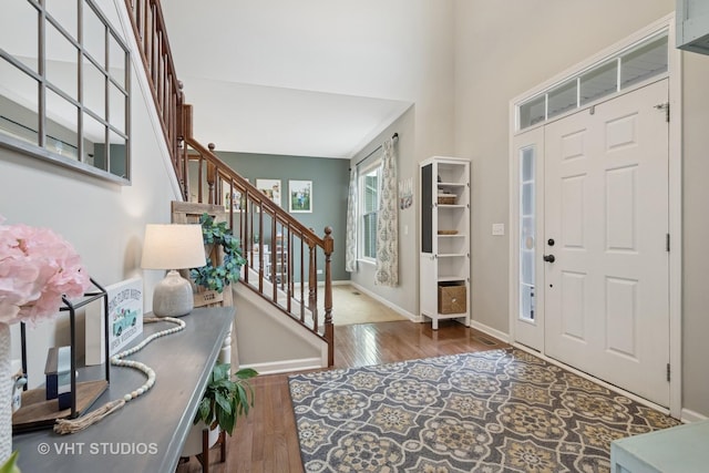 foyer entrance with baseboards, stairs, a towering ceiling, and wood finished floors