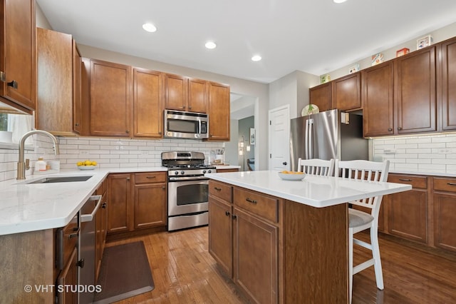 kitchen featuring decorative backsplash, a kitchen breakfast bar, dark wood-type flooring, a sink, and stainless steel appliances