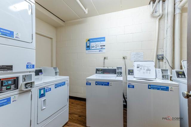 shared laundry area featuring stacked washer and dryer, concrete block wall, washing machine and dryer, and wood finished floors