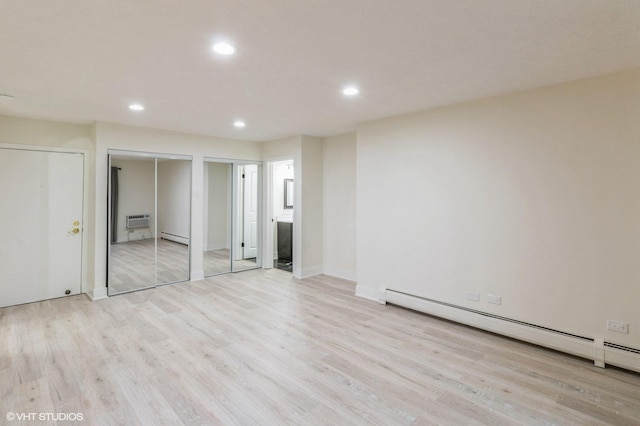 unfurnished bedroom featuring light wood finished floors, a baseboard heating unit, and two closets