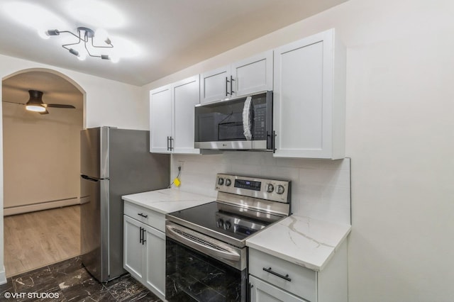 kitchen with light stone countertops, ceiling fan, appliances with stainless steel finishes, a baseboard radiator, and tasteful backsplash