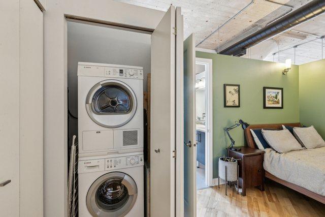 washroom featuring stacked washer / drying machine, wood finished floors, and laundry area