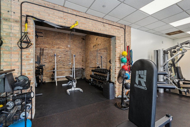 gym featuring brick wall and a drop ceiling
