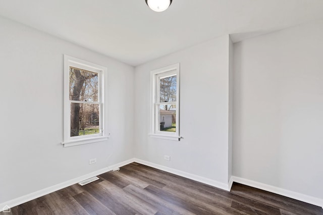 empty room featuring baseboards, dark wood-style floors, and visible vents