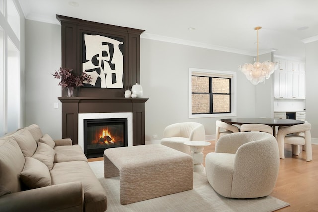 living room featuring a chandelier, light wood-style floors, a glass covered fireplace, baseboards, and ornamental molding