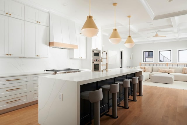kitchen with a sink, a breakfast bar, open floor plan, light wood-type flooring, and a center island with sink