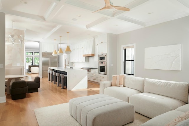 living area featuring beamed ceiling, coffered ceiling, a ceiling fan, and light wood-type flooring
