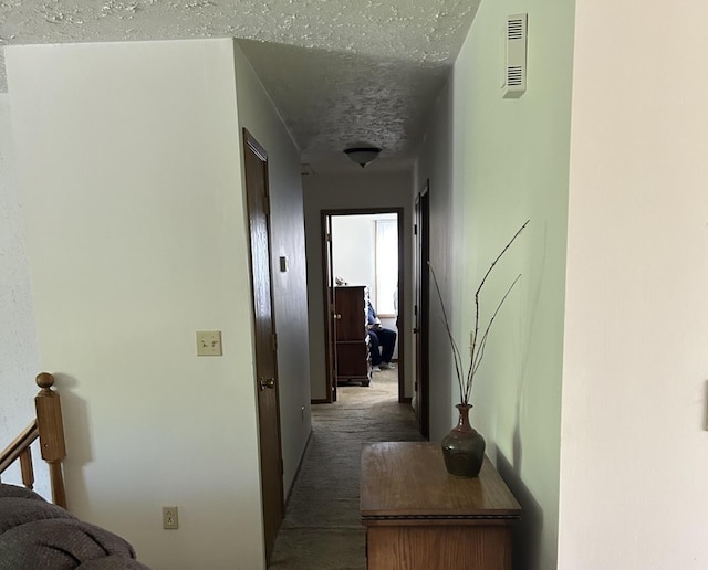 corridor with a textured ceiling, visible vents, and carpet