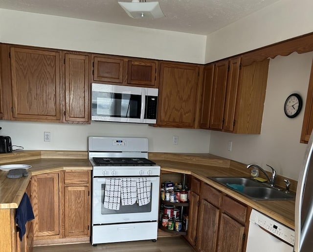 kitchen featuring white appliances, brown cabinets, a sink, and wood finished floors