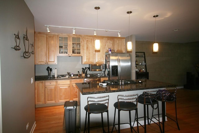 kitchen with a sink, rail lighting, light wood-style flooring, a kitchen bar, and appliances with stainless steel finishes