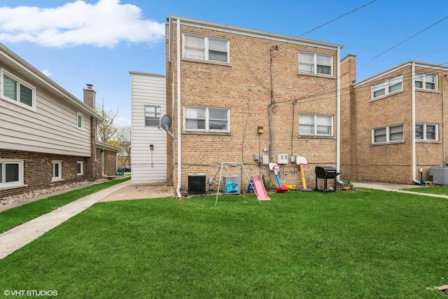 back of property featuring a lawn, central AC, and brick siding