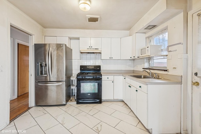 kitchen featuring stainless steel fridge, under cabinet range hood, light countertops, a sink, and black gas range