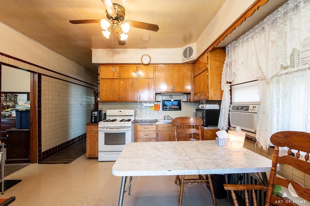 kitchen with brown cabinetry, white range with gas cooktop, a sink, visible vents, and a ceiling fan