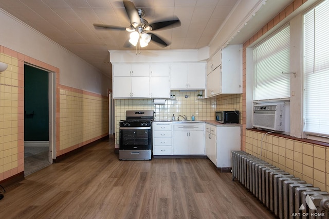 kitchen with radiator, stainless steel gas range, white cabinetry, and crown molding