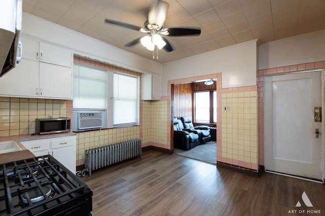kitchen with dark wood-style floors, radiator heating unit, white cabinetry, ornamental molding, and black gas range oven