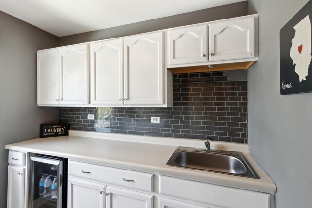 kitchen with beverage cooler, white cabinetry, a sink, decorative backsplash, and light countertops